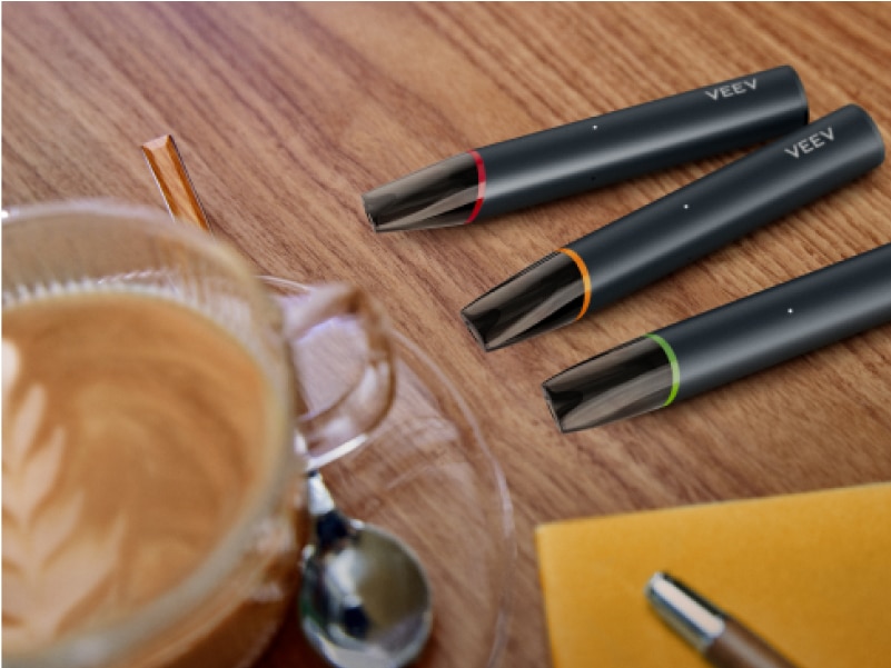 Three VEEV NOW ULTRA vapes lying next to each other on a wooden table