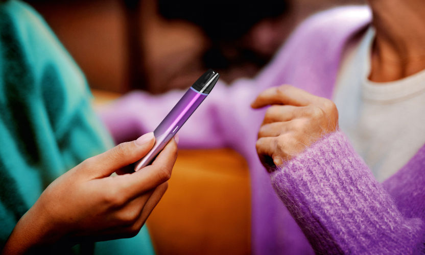Fioletowe urządzenie do waporyzacji VEEV inPRIME w dłoni osoby rozmawiającej z inną osobą