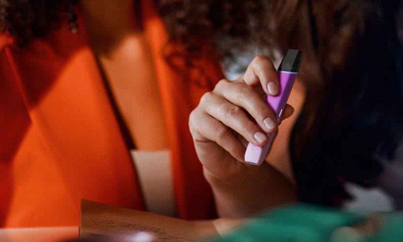 Różowo-fioletowe urządzenie do waporyzacji VEEV inPRIME w dłoni, obok osoba w pomarańczowej marynarce